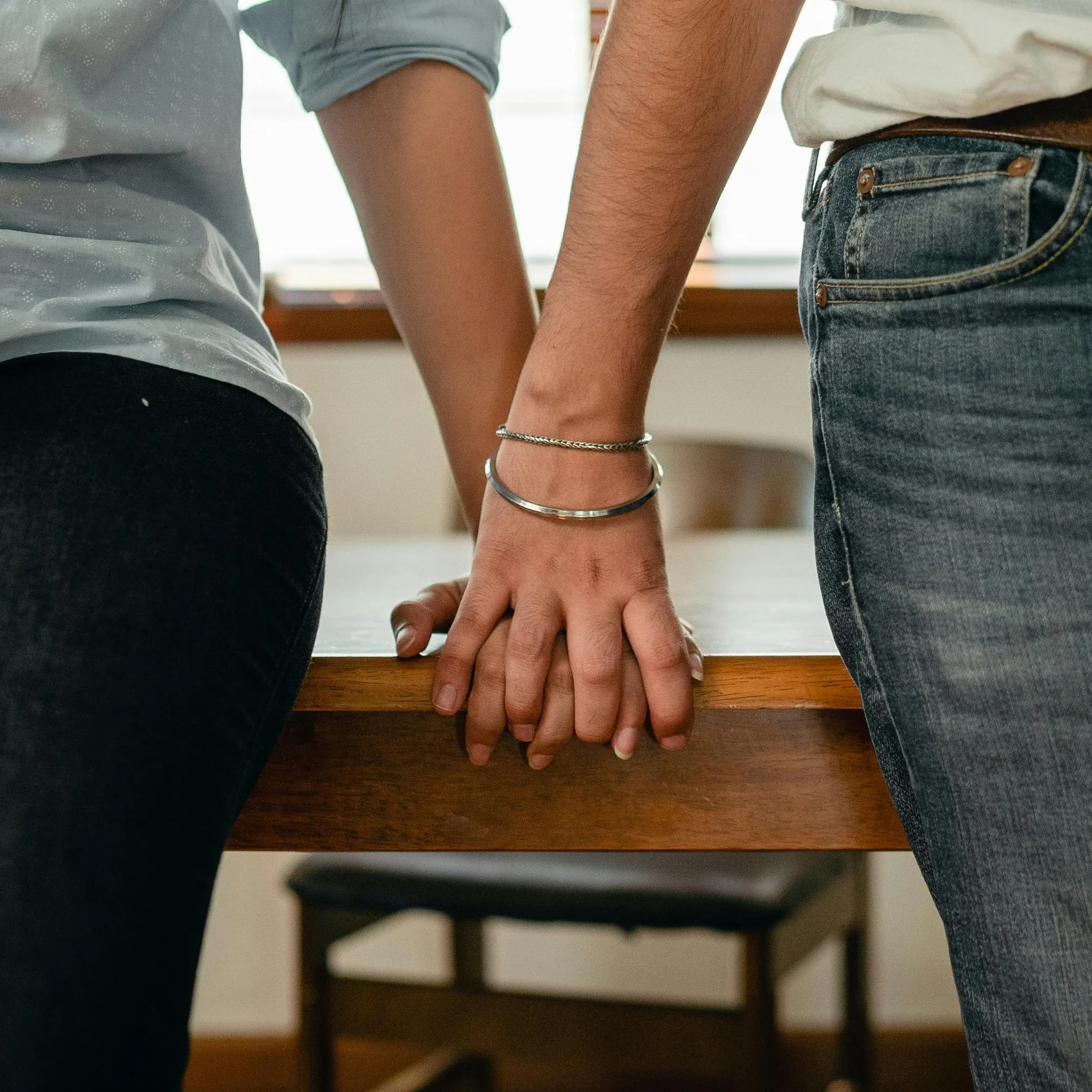 Two people standing side by side, holding hands on the edge of a wooden table