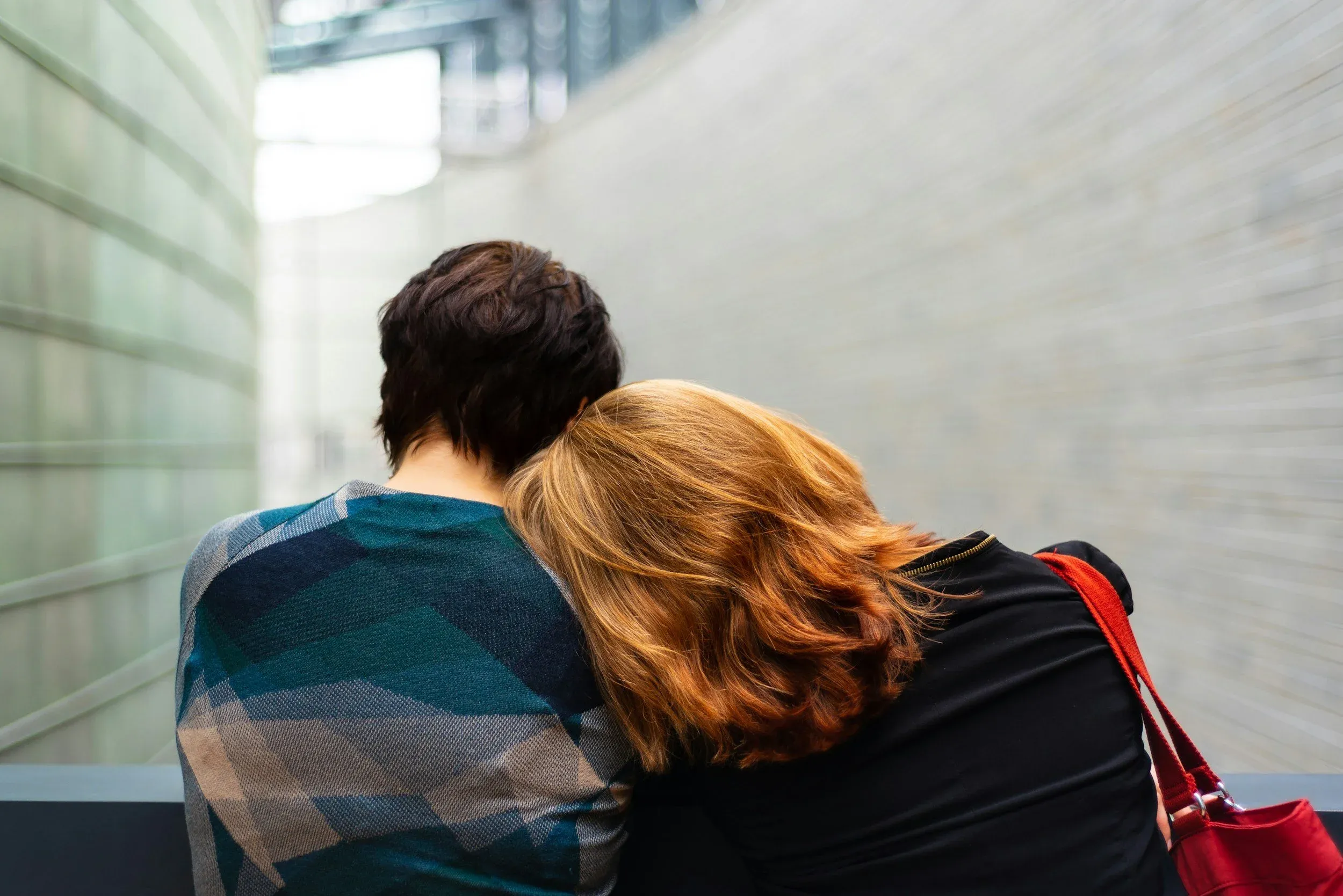 Two people seen from behind, one resting their head on the other's shoulder