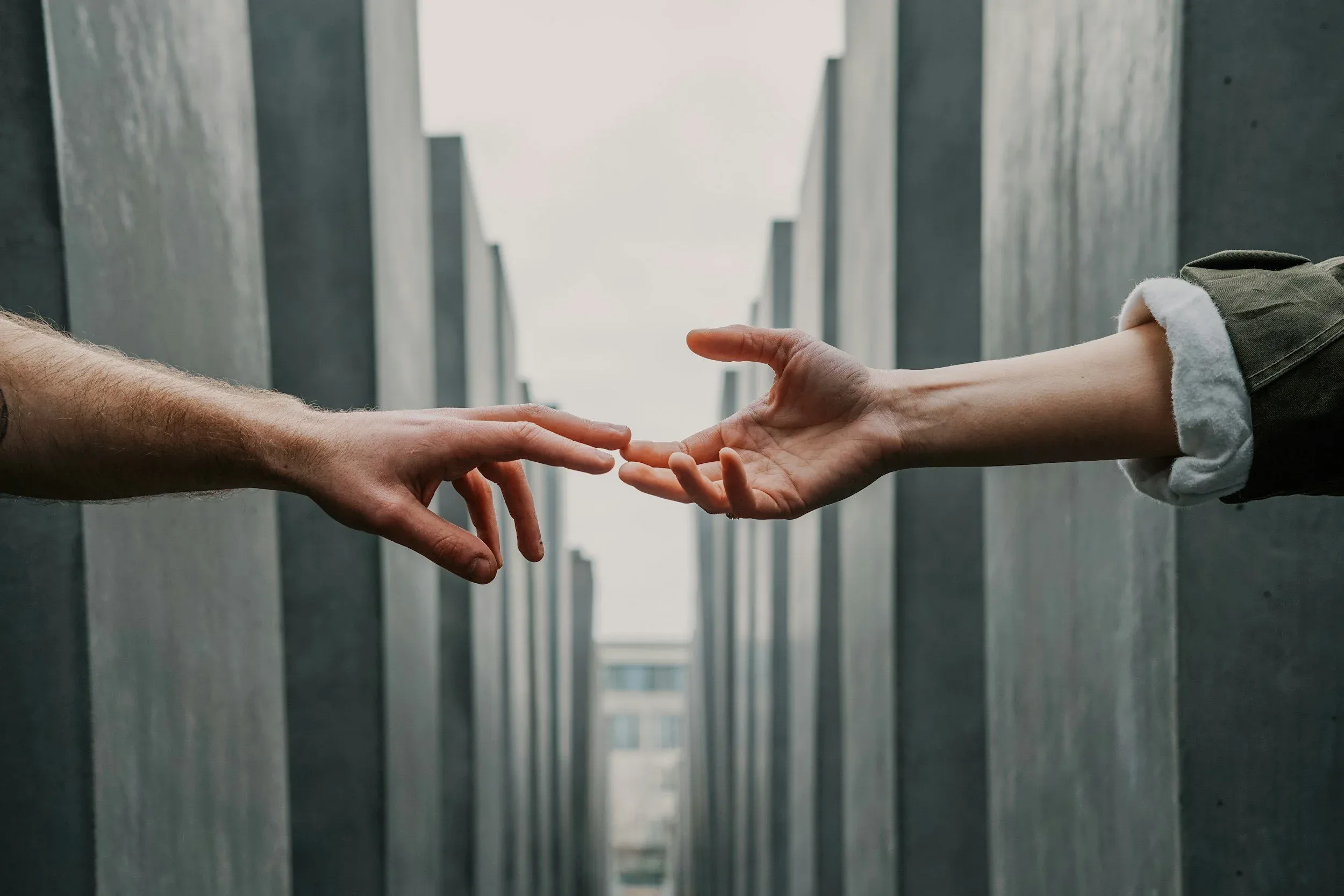 Two hands reaching towards each other between tall grey concrete pillars