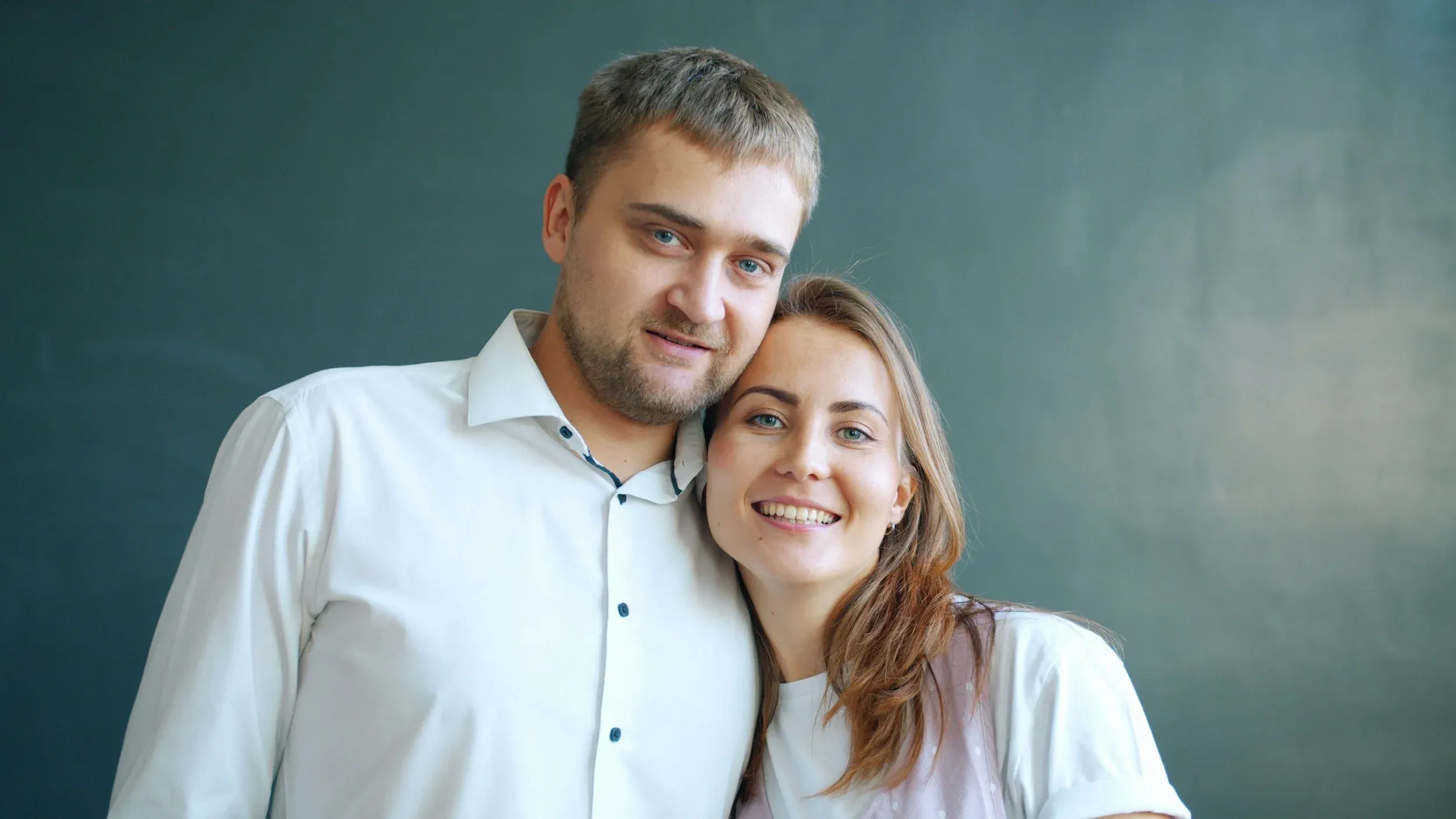 A smiling couple standing close together against a dark background
